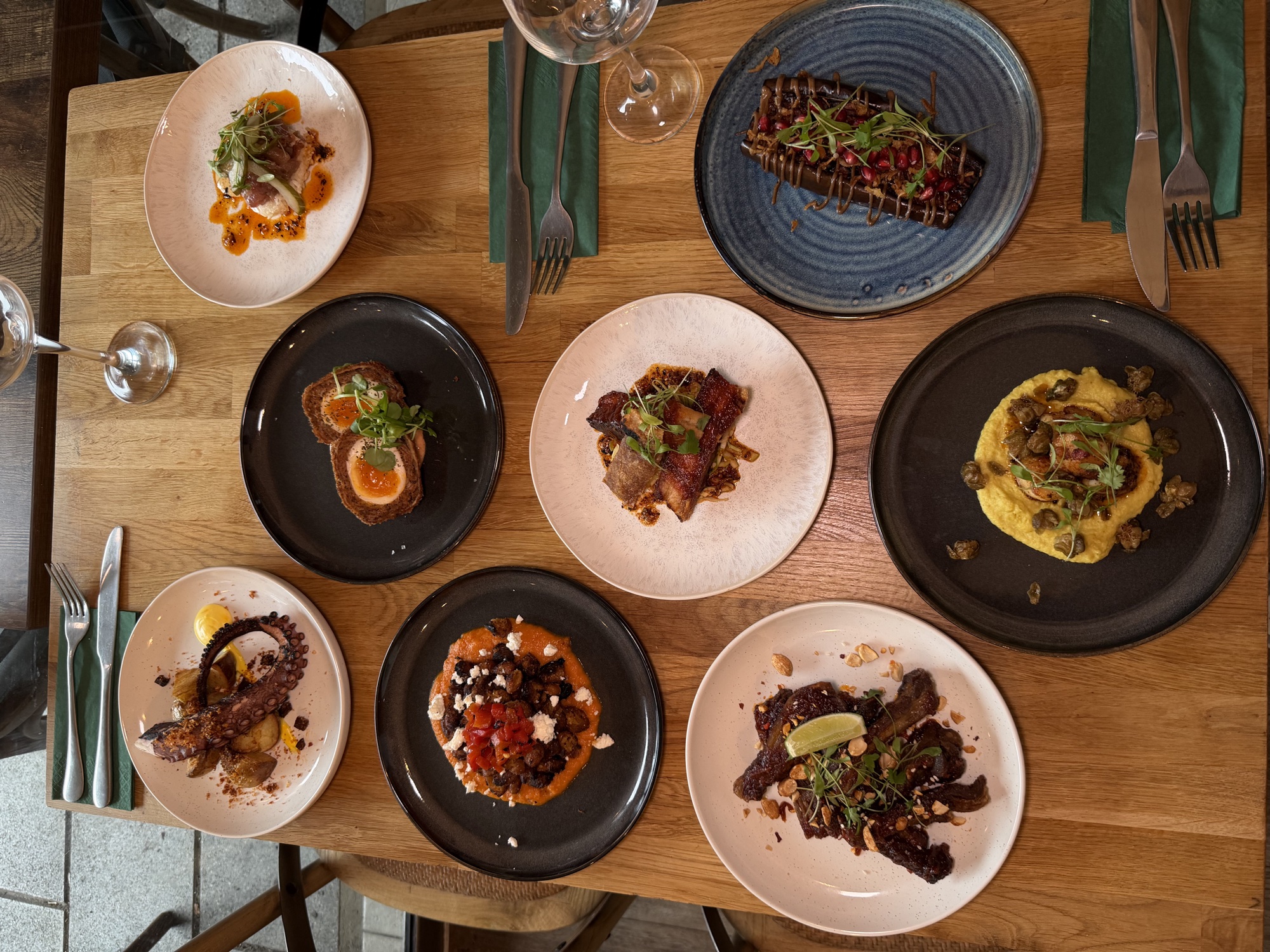 Eight small plates shared on a wooden table — octopus, scotch egg, pork belly and more