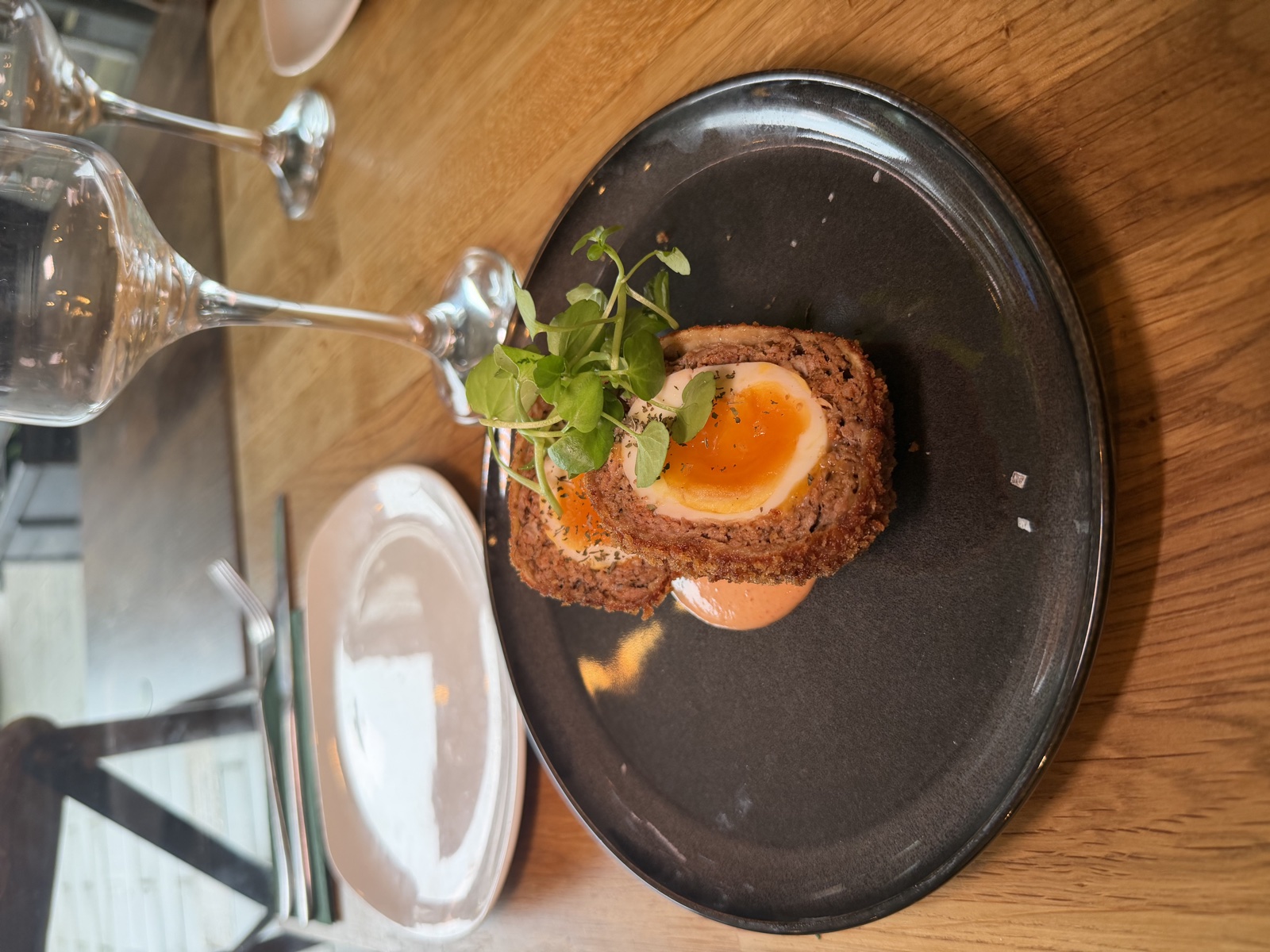 Scotch egg with jammy yolk, watercress and harissa mayo on a black plate